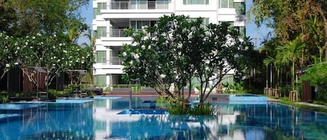 Un hotel moderno con piscina, rodeado de exuberante vegetación y un cielo azul despejado.