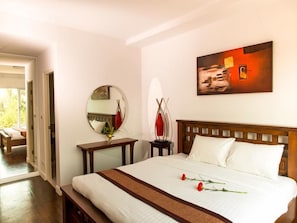 Une chambre à coucher avec un grand lit, une table de chevet ornée d’un vase, un miroir et un tableau accroché au mur.