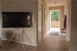 Ein Zimmer mit einem Flachbildfernseher auf einem Stativ, Holzboden und Blick auf einen Balkon mit Holzlattenzaun.