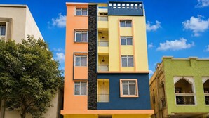 A multi-story building with a central staircase, balconies, and a tree in the foreground. - Classic fo Sunidh (Hyderabad)