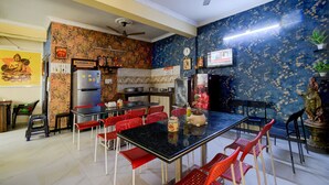 A dining area with a black table and red chairs, a ceiling fan, and a kitchen with a refrigerator and stove. - Classic fo Sunidh (Hyderabad)