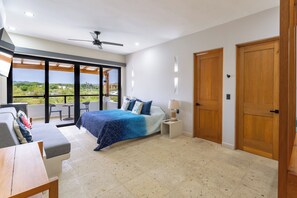 Un dormitorio con cama, mesita de noche, lámpara, ventilador de techo y vistas al exterior.