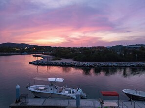 Un río tranquilo al atardecer con barcos amarrados a un muelle, rodeado de árboles y edificios al fondo.