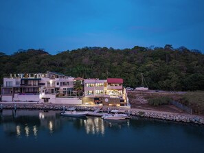 Una propietat amb vistes al mar que inclou diversos edificis, un moll amb vaixells i un turó boscos a la part de darrere.