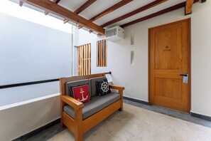 Un banco de madera con cojines, una puerta de madera y una ventana con persianas verticales.