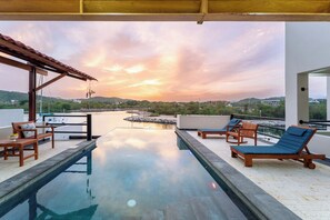 Un área de piscina en la azotea con sillones de descanso y vistas a la puesta de sol sobre el agua.