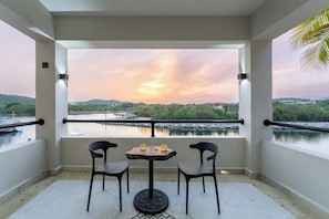 Een balkon met een tafel en stoelen, met uitzicht op een wateroppervlak en een zonsondergang.