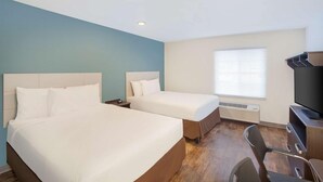 Habitación de hotel con dos camas, un escritorio, una silla y un televisor.