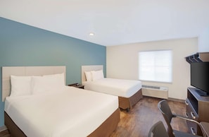 A hotel room with two beds, a desk, a chair, and a TV. - Woodspring Suites Orlando South (Orlando)