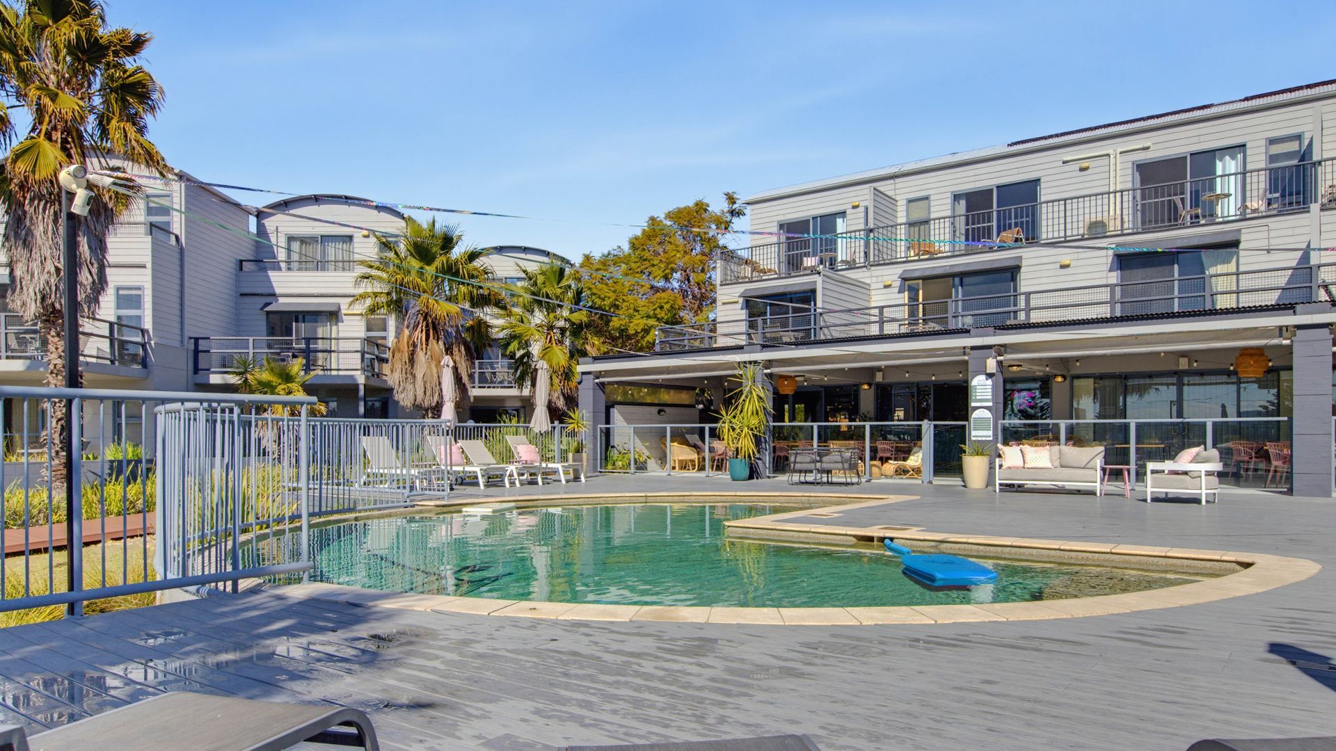 A pool area with lounge chairs and a building with balconies.