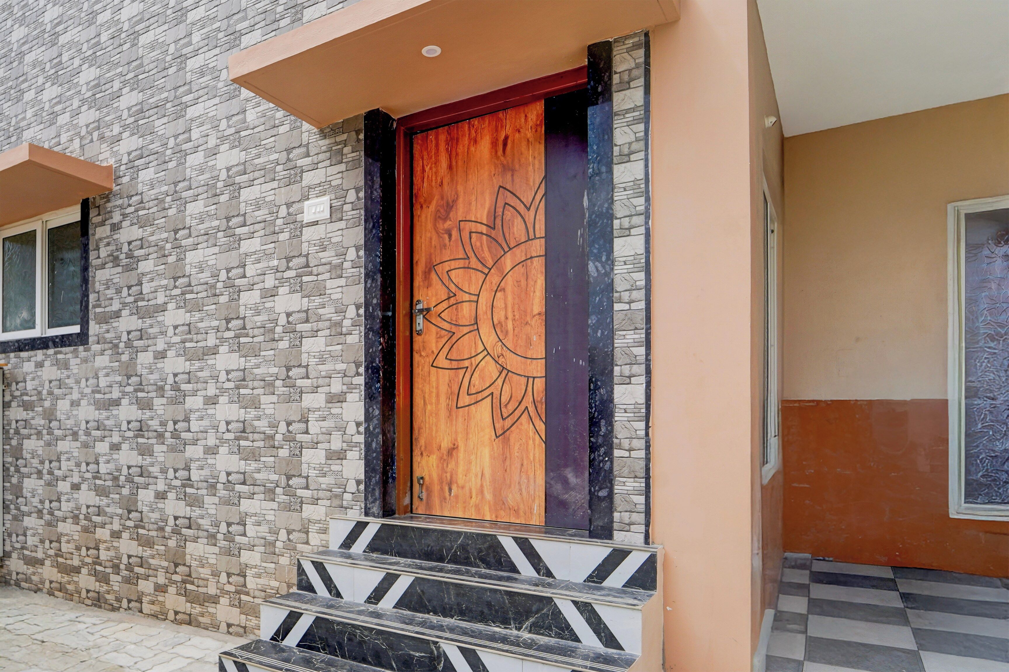A building entrance with a stone facade, a wooden door with a sun design, and a set of black and white striped steps.