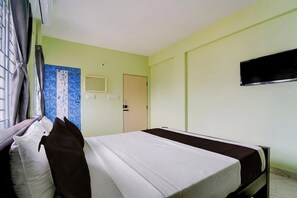 Habitación de hotel con cama, televisión montada en la pared y ventana con cortinas.