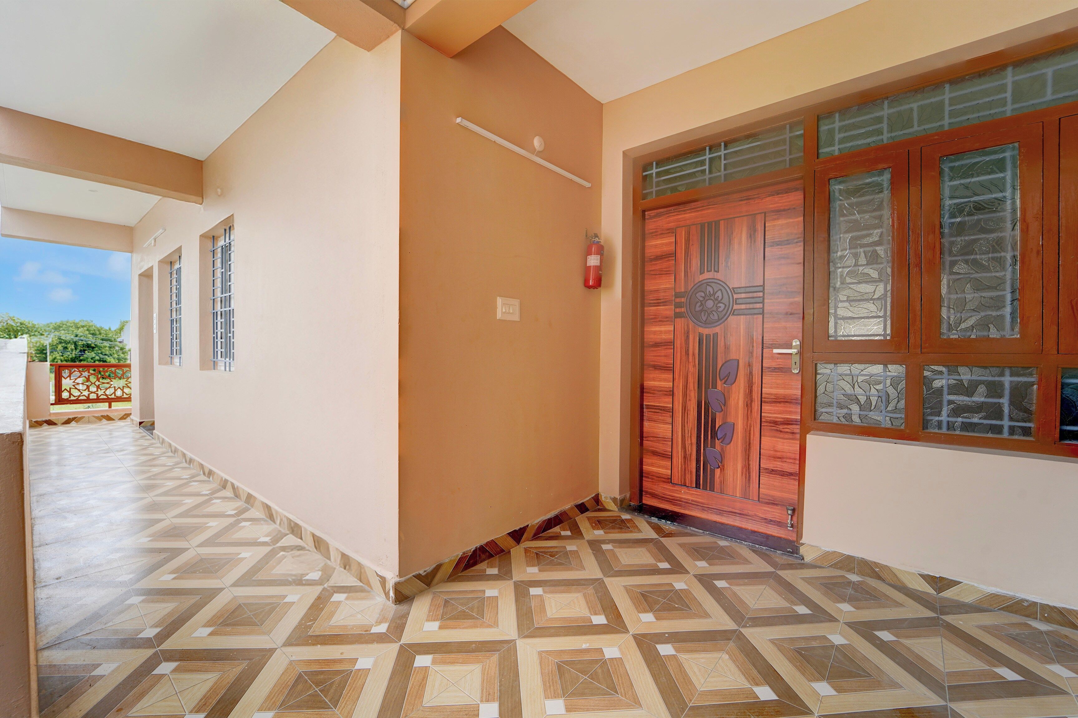 A corridor with patterned flooring, a wooden door with glass panels, and a fire extinguisher mounted on the wall.