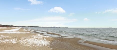 Een strand met een brede zandkust en rustig water.
