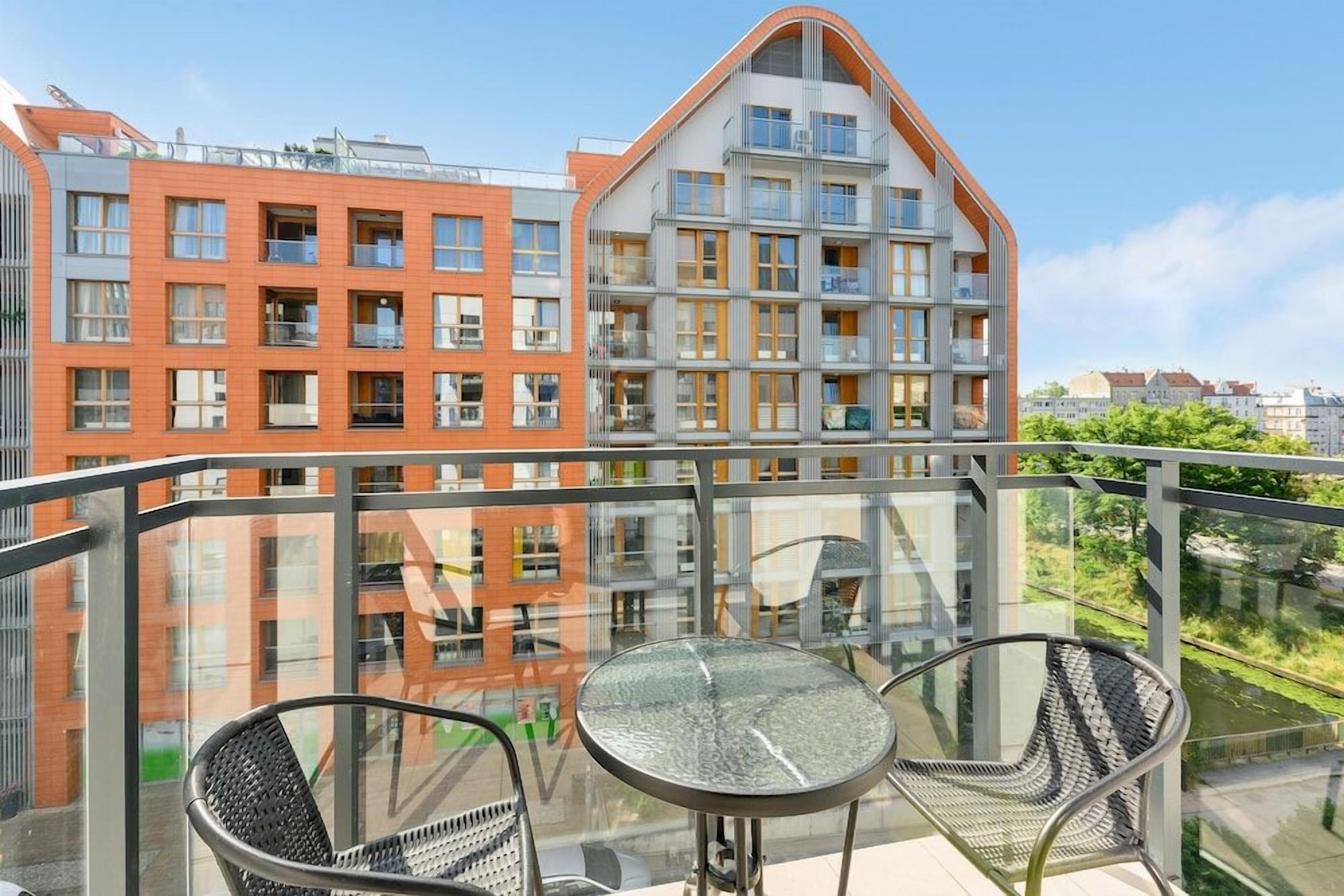 A balcony with a glass railing, two chairs, and a table.