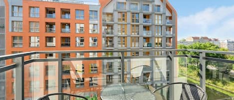 A balcony with a glass railing, two chairs, and a table.