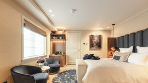 Et moderne hotelværelse med en stor seng, et siddeområde med stol og bord, et lille skrivebord og en dekorativ vægdekoration.