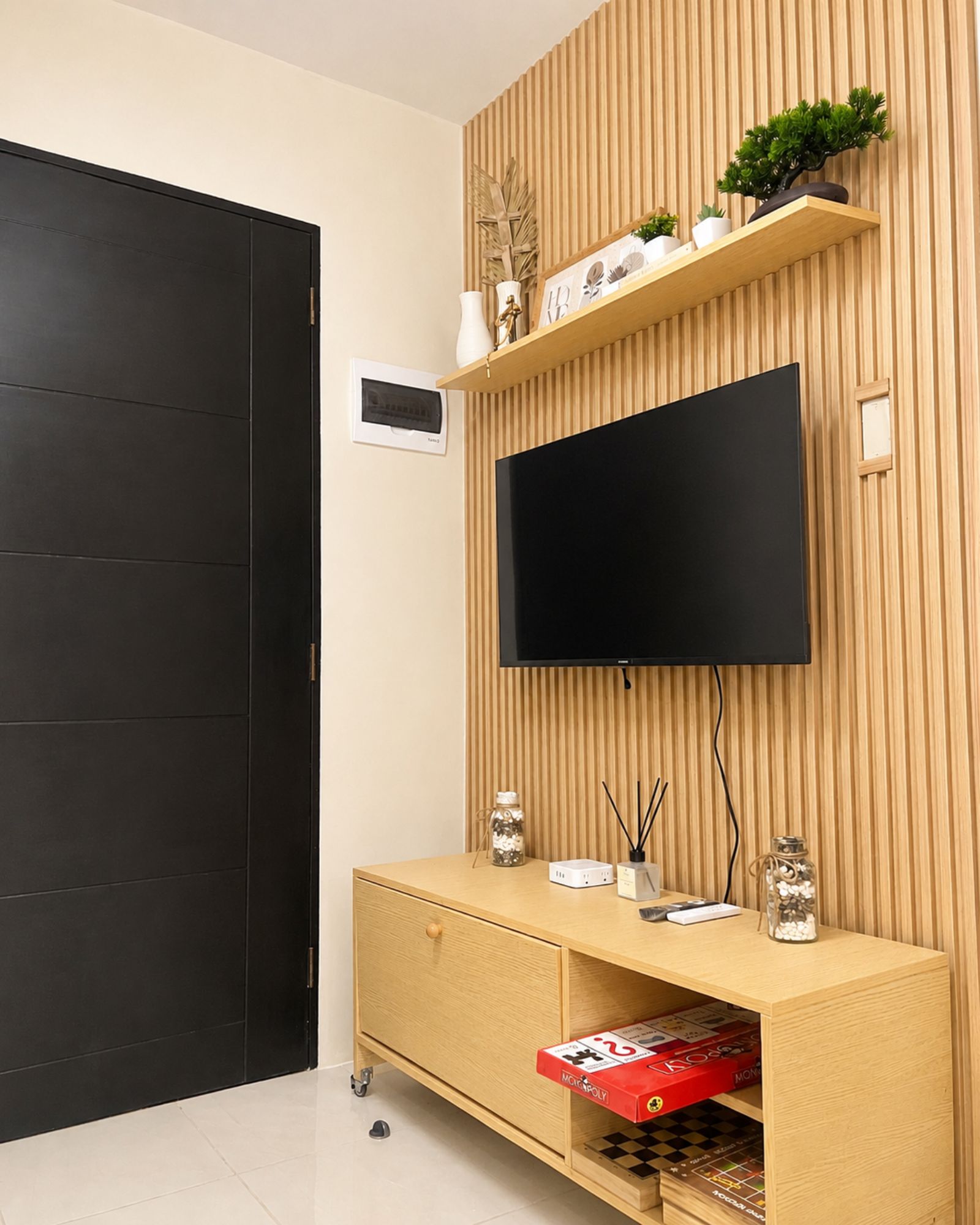 A modern living room with a flat-screen TV mounted on a wooden wall, a wooden cabinet with a TV stand, and a door.