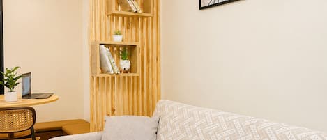 Una sala de estar moderna con un sofá, una estantería de madera, un escritorio con una computadora portátil y dos obras de arte enmarcadas en la pared.
