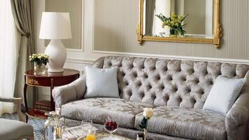 A luxurious living room with a tufted sofa, a glass coffee table with breakfast items, a side table with a lamp, and a large mirror.