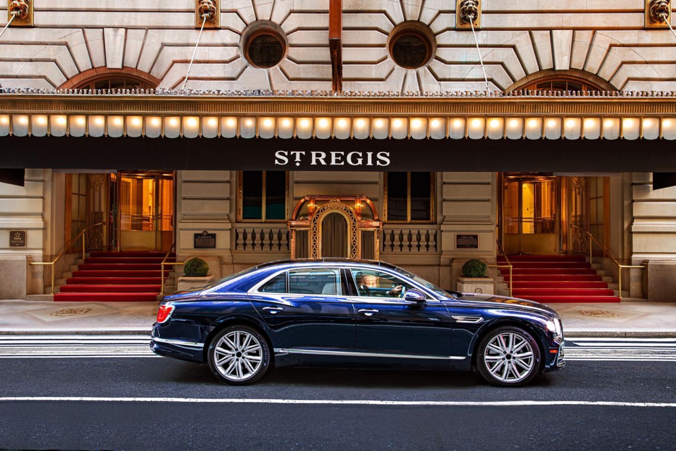 A luxury car parked in front of a grand building with a sign reading 'STREGIS'.