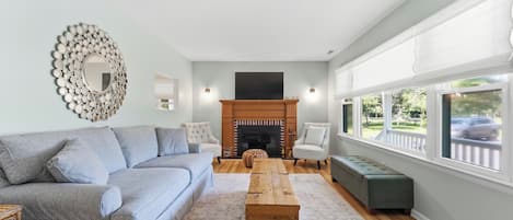 Una sala de estar con chimenea, sofá, mesa de centro y ventana con vistas al exterior.