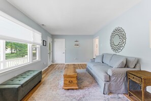 Ein geräumiges Wohnzimmer mit einem grauen Sofa, einer grünen Bank, einem Holztisch und einem Korbtisch.
