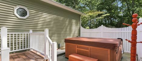 A hot tub with steps leading up to it, a white fence, and a house with siding.