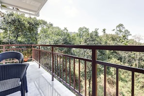 A balcony with a metal railing, a wicker chair, and a view of dense greenery. - Collection O Munnar (Devikolam)