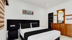 Een slaapkamer met een zwart hoofdbord, een bed met witte beddengoed, een houten garderobe en een wandplank met spiegel.