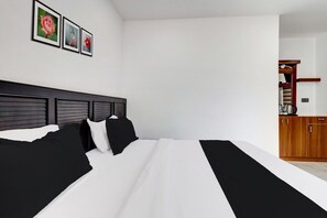 A hotel room with a bed, a wooden headboard, a kitchenette, and a wall with framed pictures. - Collection O Munnar (Devikolam)