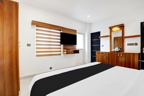 A modern bedroom with a bed, a TV mounted on the wall, wooden cabinets, and a large mirror. - Collection O Munnar (Devikolam)