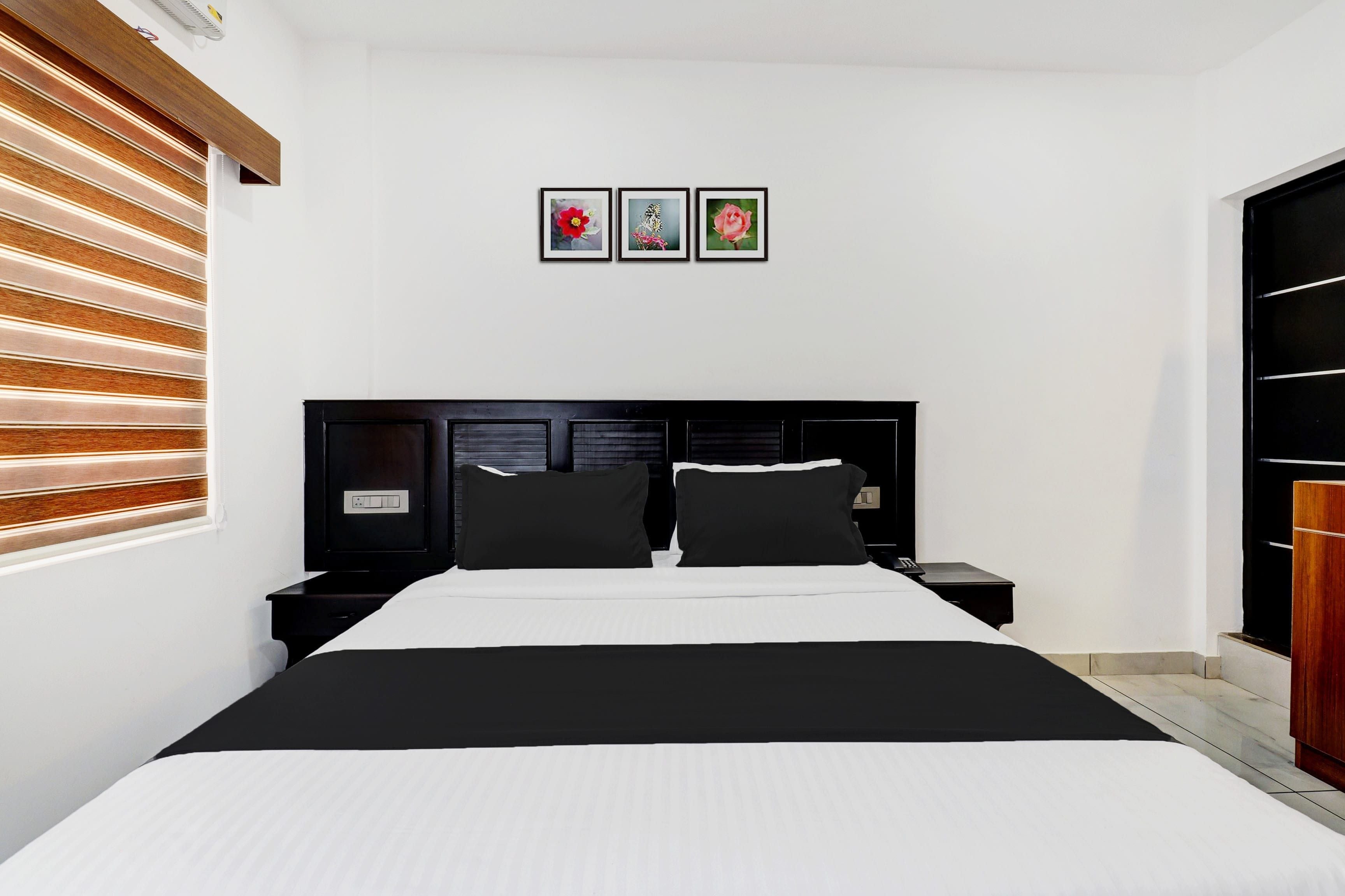 Un dormitorio con cabecera negra, cama con ropa de cama blanca, dos mesitas de noche y persiana de madera con listones.