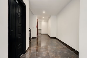 A hallway with a black door, white walls, and a marble floor. - Collection O Munnar (Devikolam)