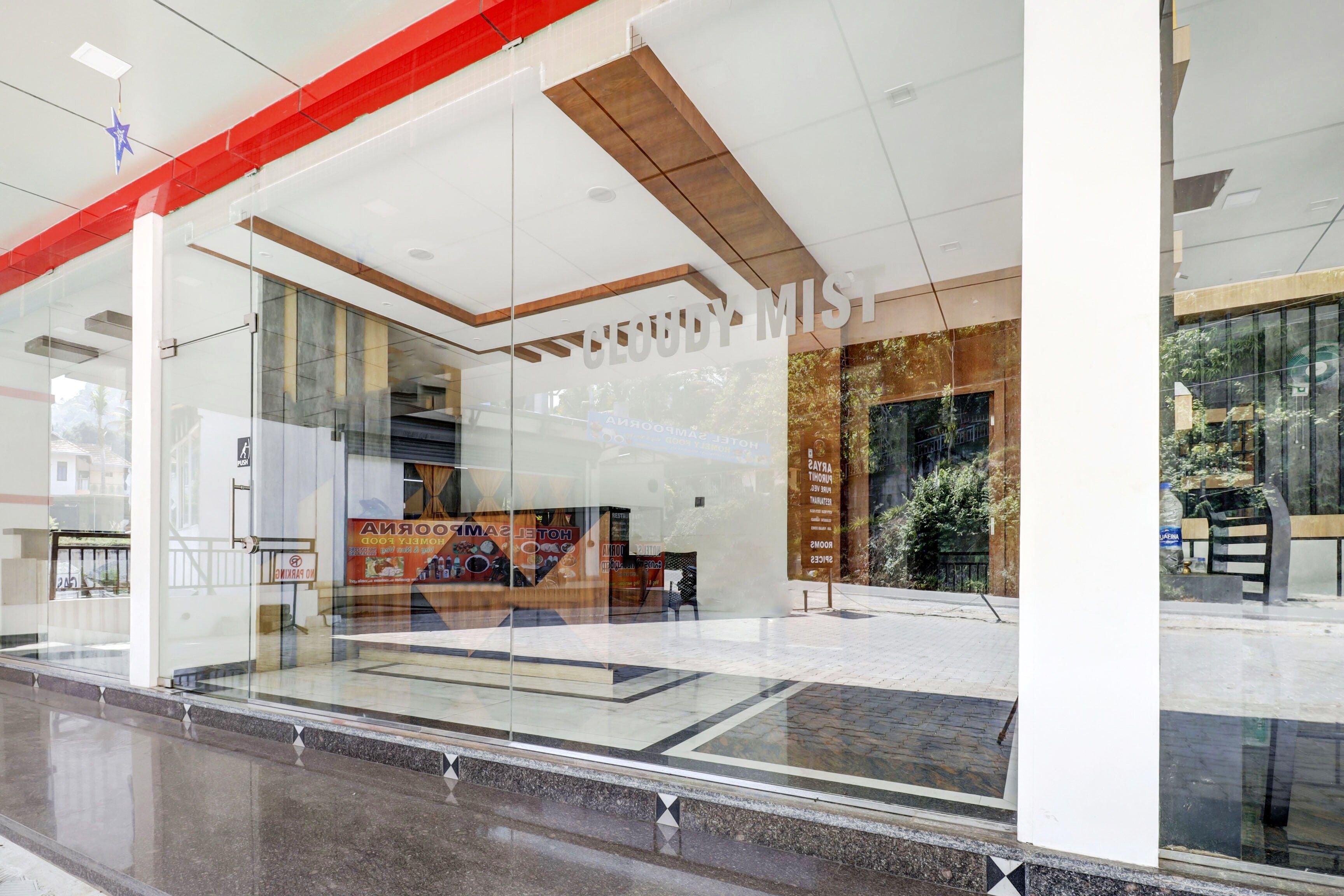 L’entrée d’un hôtel avec une façade en verre, une enseigne indiquant « CLOUDY MIST », et un reflet de l’environnement extérieur.