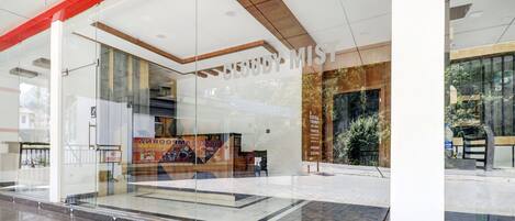 A hotel entrance with a glass facade, a sign reading 'CLOUDY MIST', and a reflection of the outside environment.