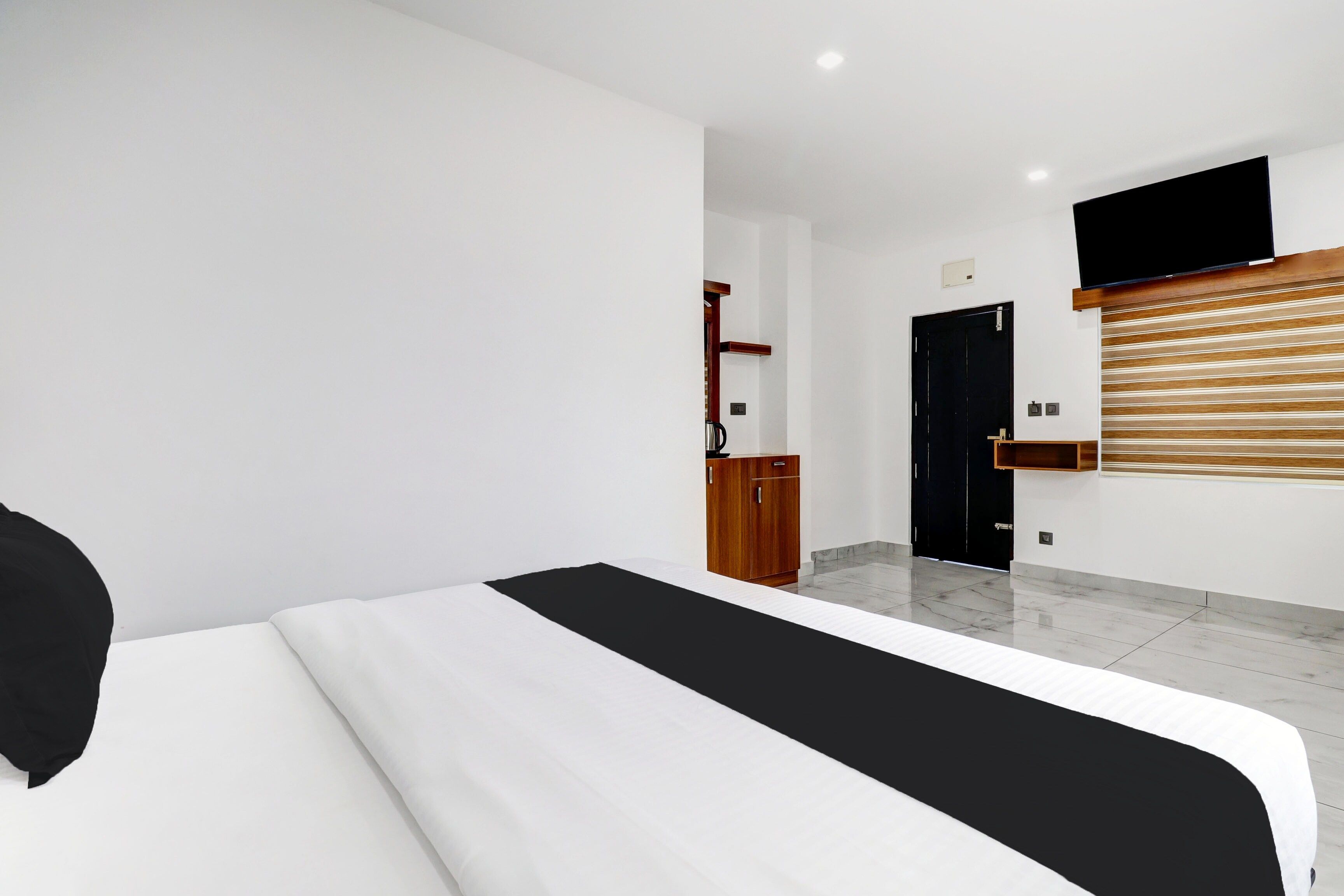 A modern bedroom with a large bed, a wooden wardrobe, a black door, and a mounted television.