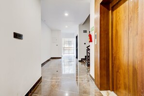 A corridor with a wooden door, a fire exit sign, and a fire extinguisher on the wall. - Collection O Munnar (Devikolam)