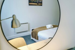 Ein Hotelzimmer mit Bett, Nachttisch, Lampe, Heizkörper und einem Gemälde an der Wand.