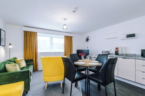 Ein modernes Wohnzimmer mit einem grünen Sofa, gelben Sesseln und einem Esstisch für vier Personen.