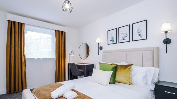 Habitación de hotel con una cama, un escritorio, una silla, un espejo y dos lámparas de pared.