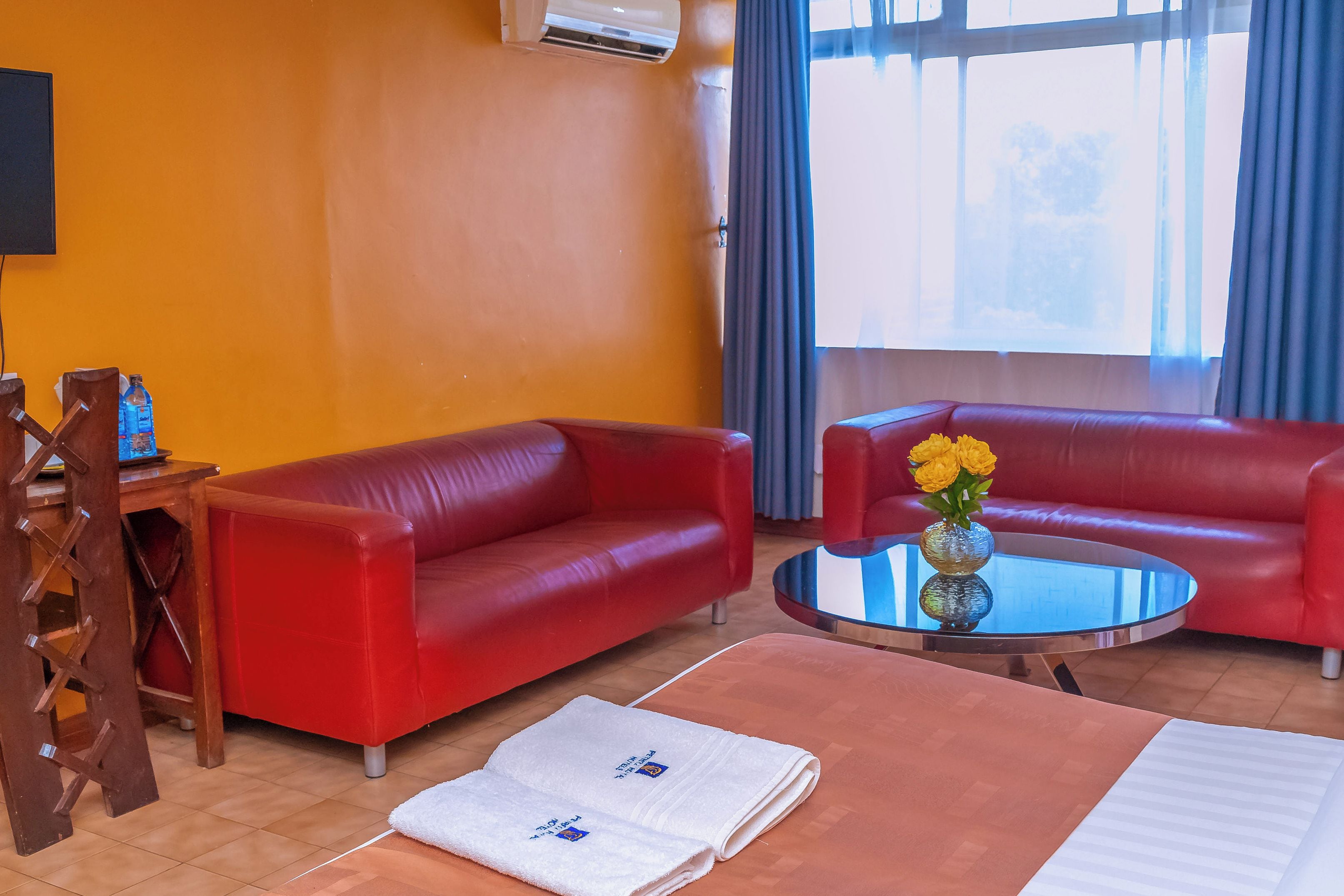 Una habitación con dos sofás de cuero rojo, una mesita redonda con un jarrón de flores amarillas, una toalla blanca y una silla de madera.
