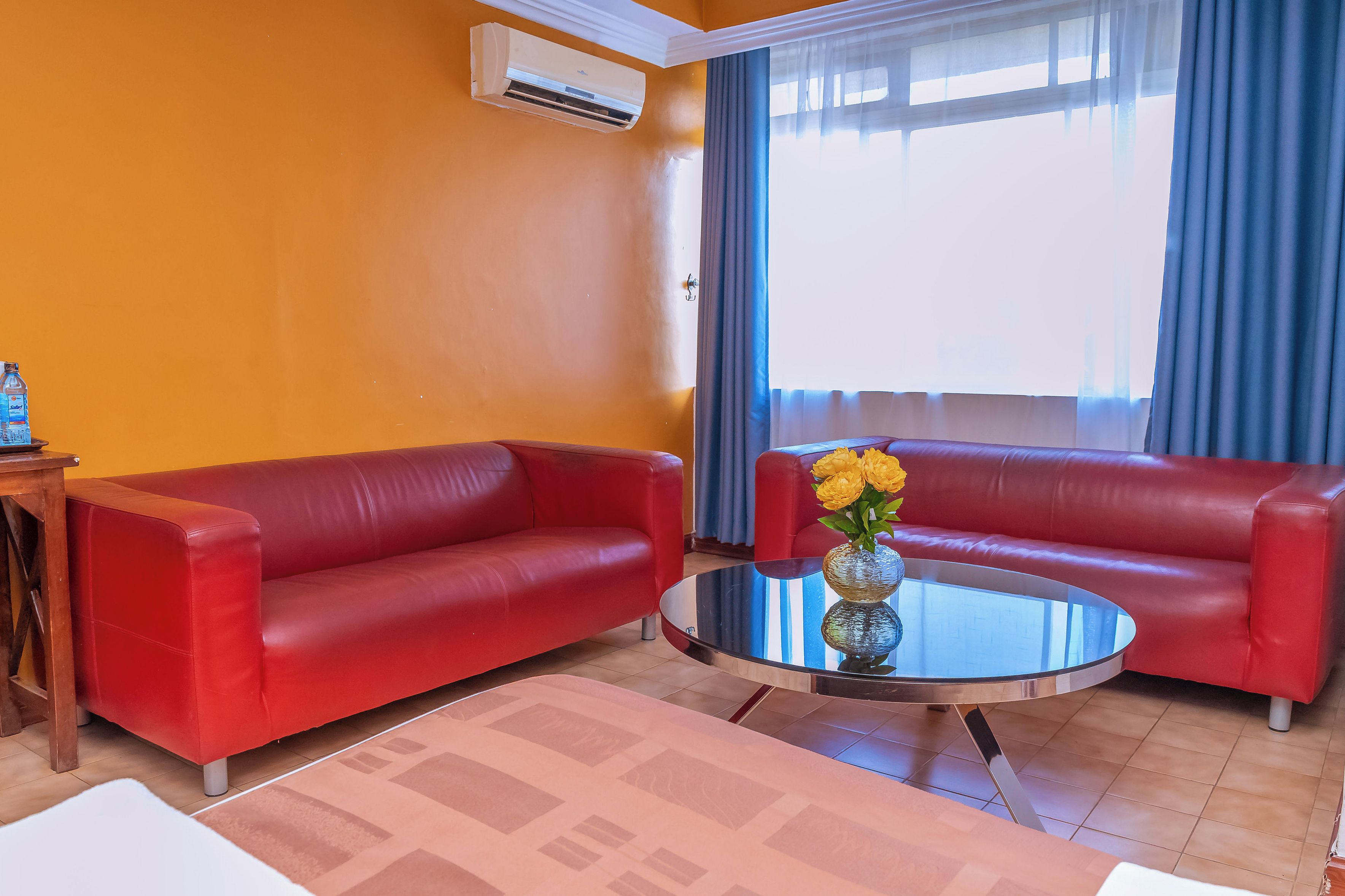 Un salon avec deux canapés rouges, une table basse en verre et un vase rempli de fleurs jaunes.