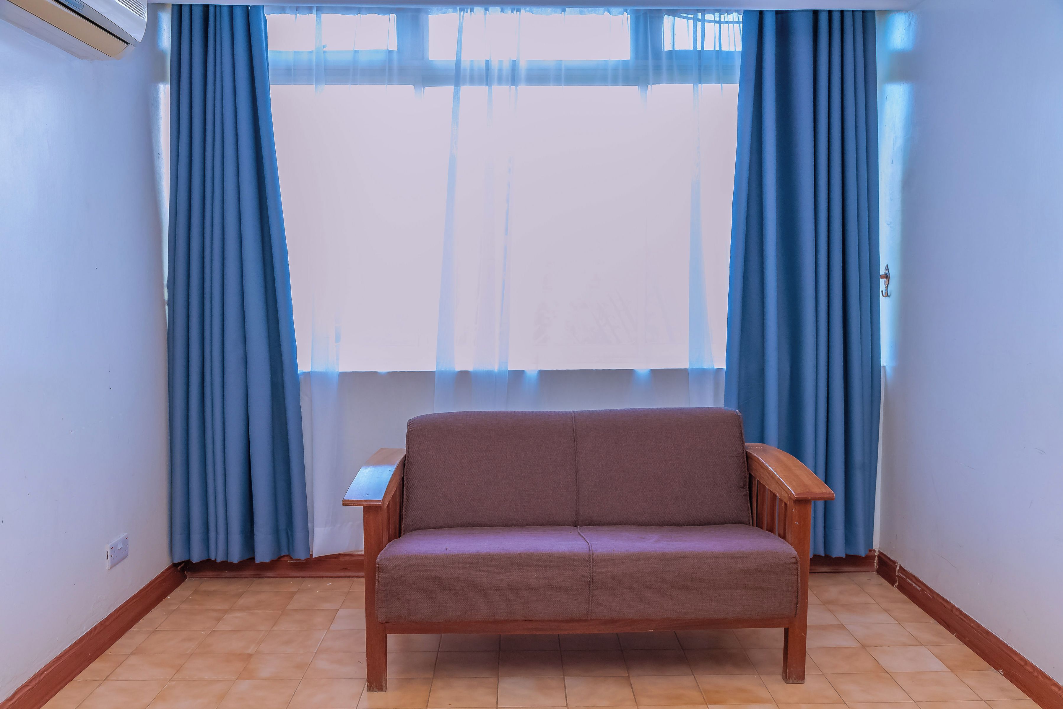 A room with a sofa, a window with curtains, and a tiled floor.