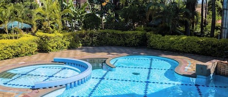 Una piscina con diseño de mosaicos, rodeada de vegetación y un edificio al fondo.