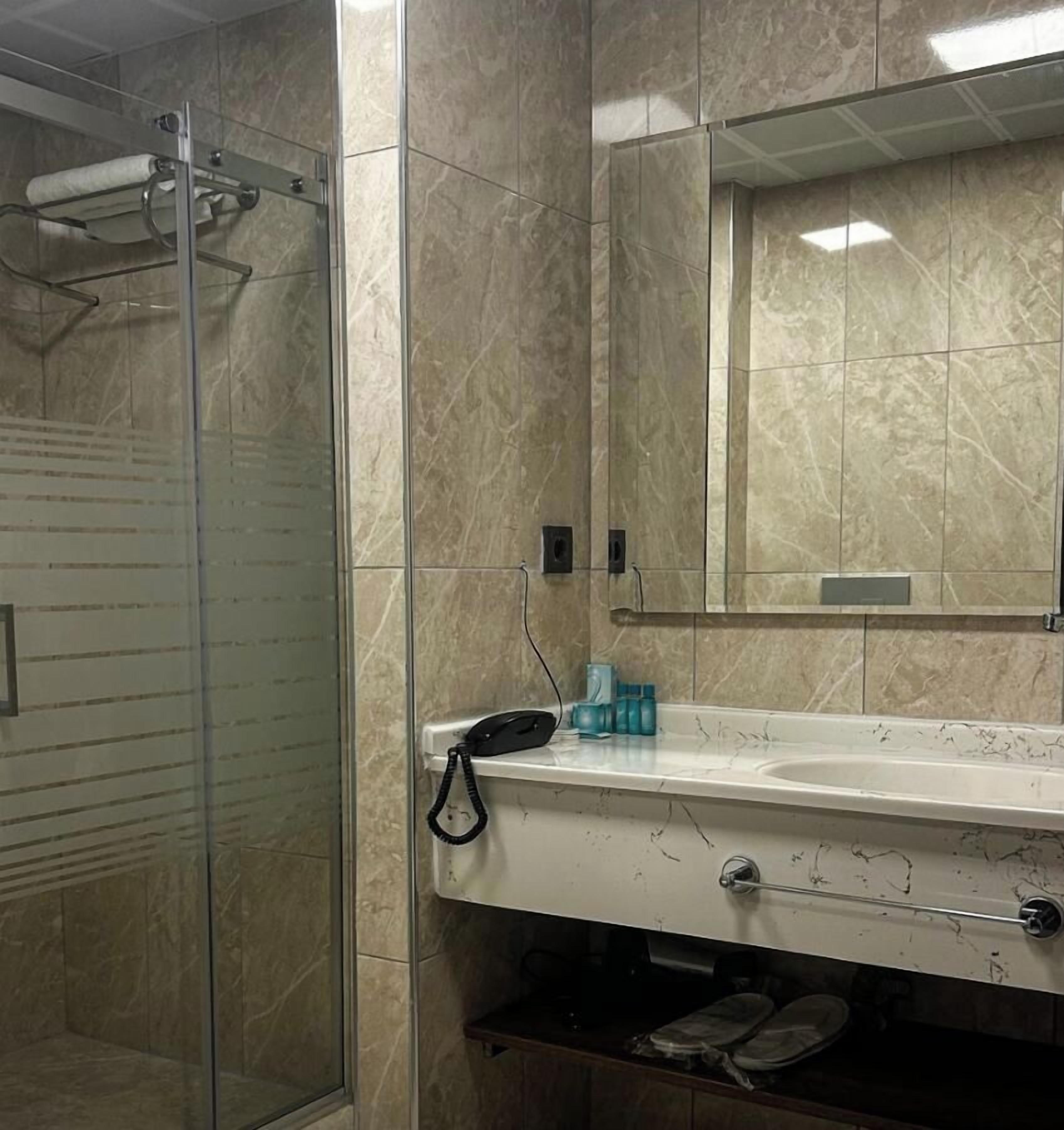 Un baño con ducha envuelta en vidrio, un lavabo blanco con espejo y pared con azulejos de mármol.