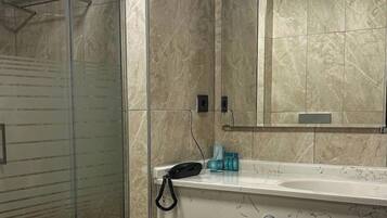 Un baño con ducha envuelta en vidrio, un lavabo blanco con espejo y pared con azulejos de mármol.