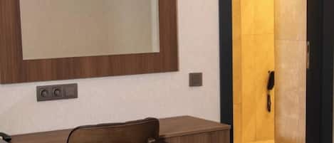 A hotel room with a bed, a desk, a chair, a large mirror, and a door leading to a bathroom.