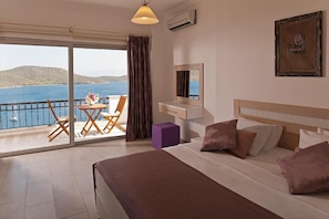 A hotel room with a bed, a desk, a chair, a small table with a vase, and a view of the sea. - Aktur Residence (Bodrum)