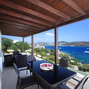 A covered outdoor seating area with a table and chairs, overlooking a coastal landscape with buildings and the sea. - Aktur Residence (Bodrum)